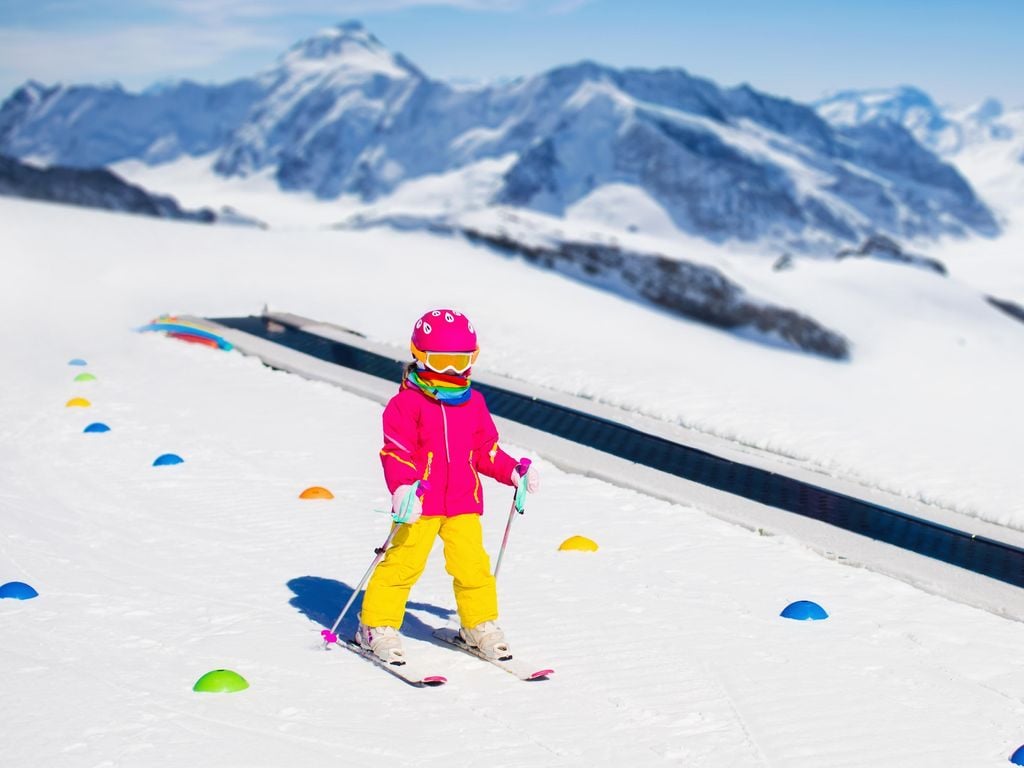 Child in alpine ski school with magic carpet lift and colorful training cones going